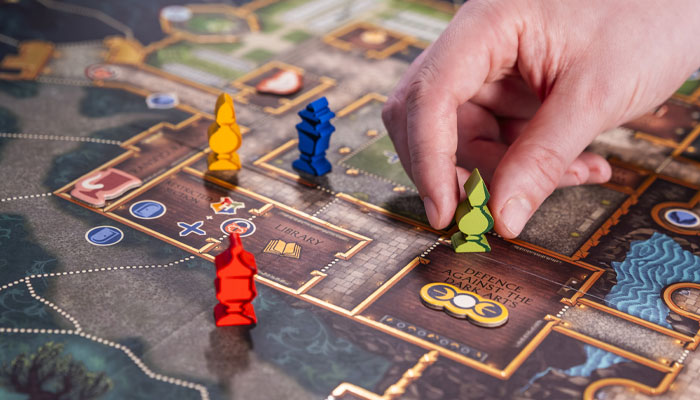 A hand moves a green House pawn on the Defenders of Hogwarts board, beside other coloured pawns